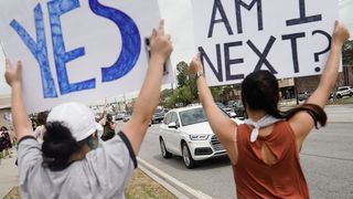 Photo of two protesters, one holding a sign that says "Am I next?" while the other holds a sign that says "Yes"